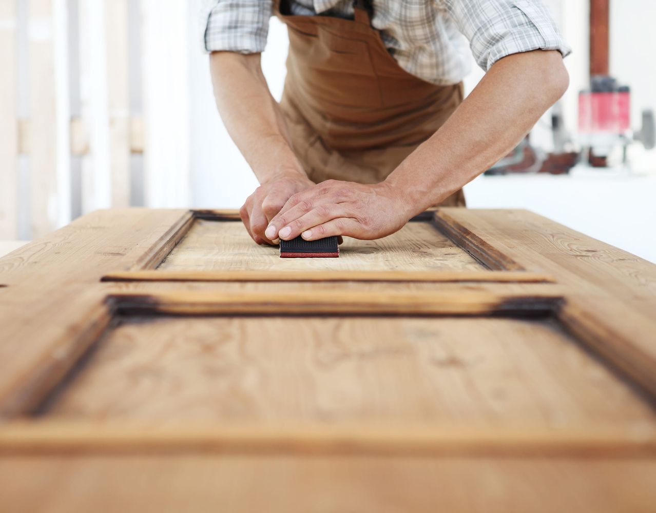 Handwerker mit Lederschürze schleift eine Holztür mit Schleifklotz von Hand